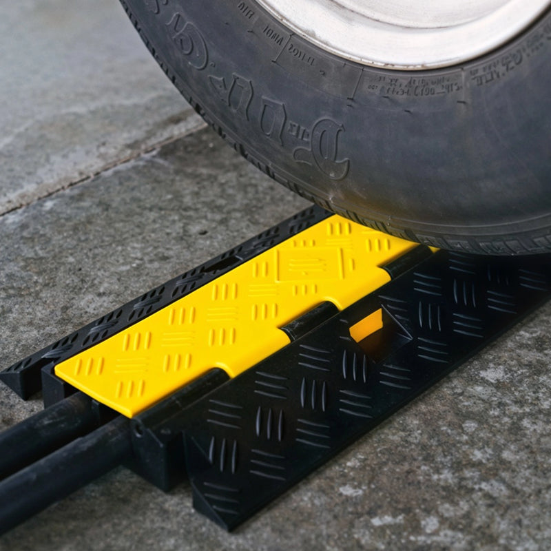 Cargue la imagen en el visor de la galería, Rampa protectora de cables de 2 canales. Neumático de automóvil transitando sobre una rampa protectora de cables de alta resistencia instalada en el suelo.
