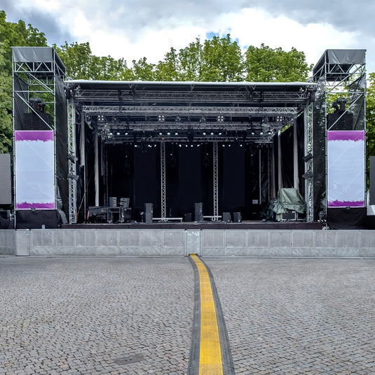 Rampa protectora de cables de 2 canales. Rampa protectora de cables instalada a lo largo del suelo de adoquín frente a un escenario de eventos al aire libre.